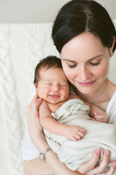 Portrait of a mother embracing her smiling newborn baby.