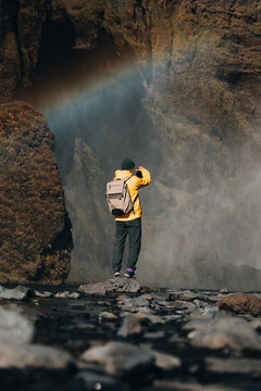 Hiker in yellow raincoat  taking picture of waterfall,vibrant rainbow