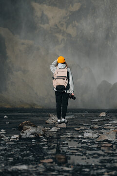Woman hiker with backpack standing at waterfall mist holding camera