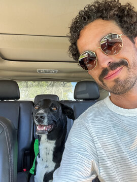 A happy man with sunglasses takes a selfie with his dog in his car