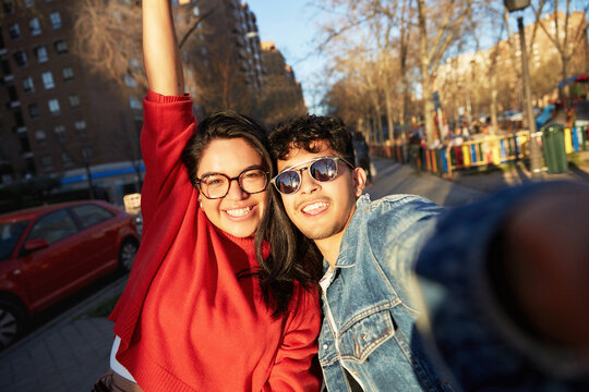 Two smiling Latino friends are taking a selfie during sunset