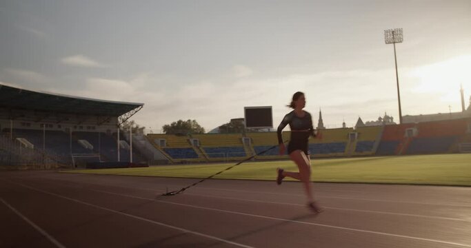 Strong female sprinter running with weights in stadium