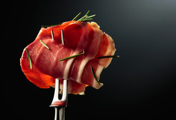 Sliced prosciutto with rosemary on a fork.