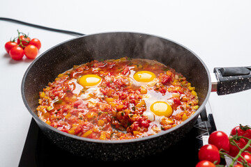 The cook puts three eggs in a Pan with Chopped Bell Peppers, Tomatoes and Onions, which are fried on the Stove. Recipe and cooking process for Shakshuka and Menemen. Step by step. Fourteenth photo.