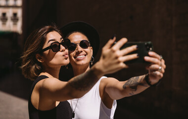 Cheerful young girlfriends taking selfie on street
