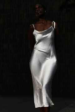 women's body in a white tight silk dress in dark background 