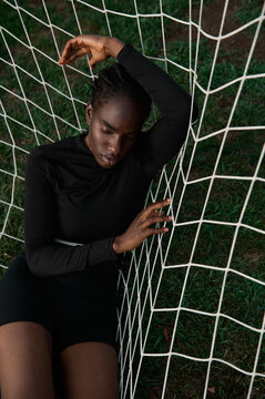 African American woman lies in a football goal net on the field 