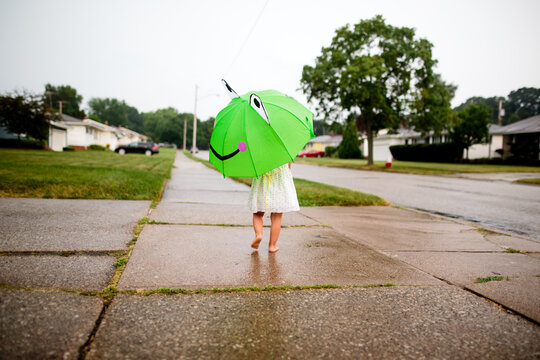 Little girl walks down sidewalk with green umbrella