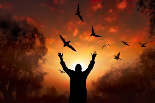Silhouette islam man open two empty hands with palms up and birds flying over autumn sunset background