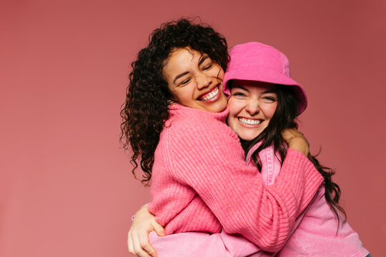 Trendy female friends having fun together against pink wall