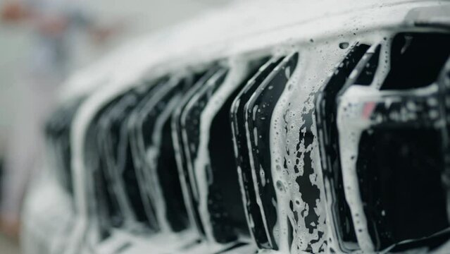 soap and water falls between twin kidney grille of a car forming an interesting little cascade with reflections. close up