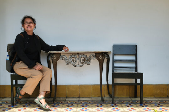 A middle-aged woman in black shirt is sitting on a wooden chair; happy expression