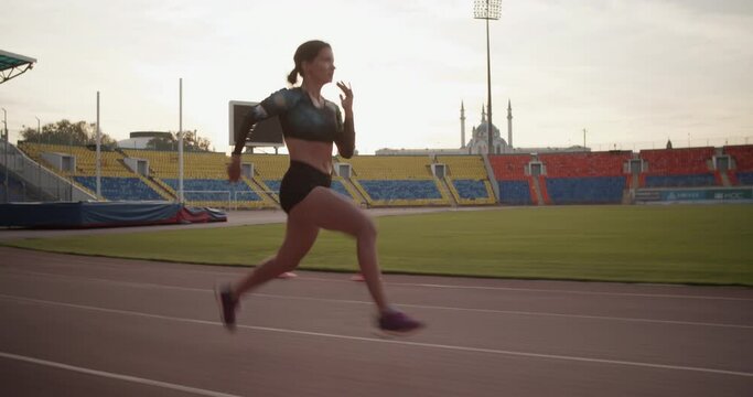 Fit female sprinter running fast in stadium during morning training