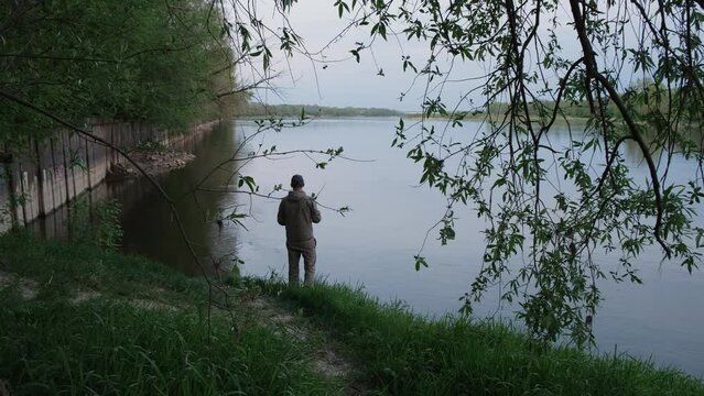 A man is fishing on the banks of a large river.