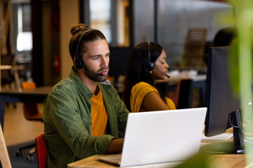 Diverse male and female creative colleague in phone headsets using computers in casual office