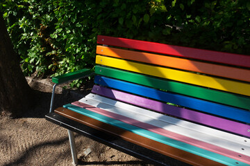 A bench painted with rainbow colours in a park