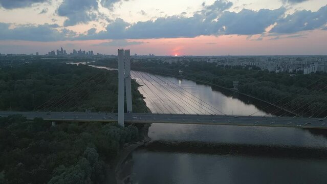 Beautiful panoramic aerial drone view to cable-stayed Siekierkowski Bridge over the Vistula river and Warsaw City skyscrapers, Poland in June dusk hour evening. The drone flies along the bridge.