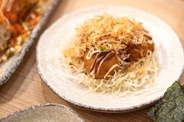 A dish of octopus takoyaki is served on wooden table. Japanese food menu object, selective focus.