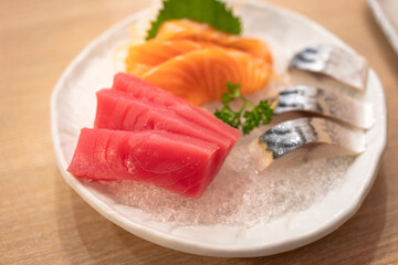Set of raw freshness sashimi in various sliced kind of fishes are served in white ceramic bowl and placed on wooden table. Japanese food meal photo, selective focus.
