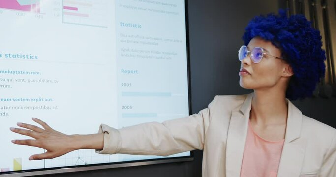 Biracial casual businesswoman with blue afro making presentation in office, slow motion