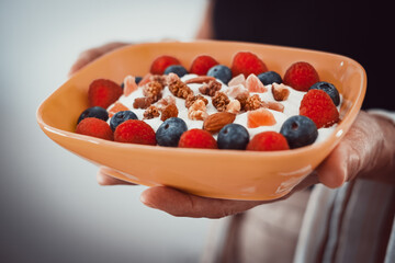Waitress woman hand holding bowl of yogurt and fresh and dried fruit with almond, raspberries, blueberries. Breakfast or lunch, eat healthy and dietary