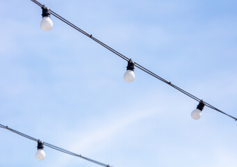 Obraz premium electric light bulbs on a wire against the blue sky in the city
