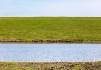 Spring landscape with a pond in the middle of green grass and blue sky