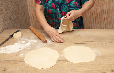 Elderly woman kneading dough on a wooden table in the kitchen