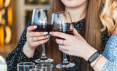 Close up of two female hands holding glasses of red wine in restaurant