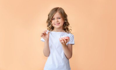 A child holds a wooden toy model of a human jaw close-up and a wooden tooth in the other hand on a beige background. Children's dentistry. Healthy baby milk teeth and gums. copy space