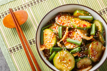 Spicy Korean cucumber salad in kimchi sauce with sesame seeds in a bowl with chopsticks on the table. Horizontal top view from above