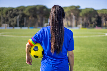 Female soccer player wearing a captain armband with the LGBT pride flag on the field. Campaign against homophobia in football. LGBTQ people in sport concept. Women's Football. Gay pride day and month.