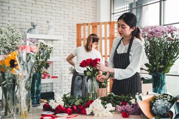 Two beautiful florist meticulously arrange red roses in glass vases for customers in the flower shop.