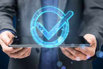 Close up of businessman hands holding pad with glowing blue polygonal checkmark on dark blurry...