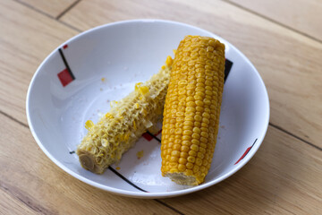 Corn cobs after cooking, one cob eaten and the other full on the plate.