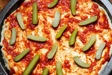 Pickled cucumbers laid out on a pizza crust covered with tomato sauce. Cooking pizza with pickled cucumbers.