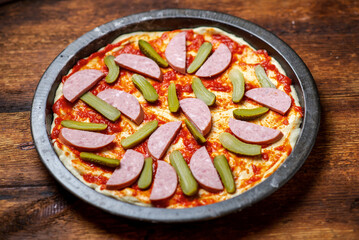 Pickled cucumbers laid out on a pizza crust covered with tomato sauce. Cooking pizza with pickled cucumbers.