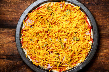 Raw pizza on a wooden background. Pizza sprinkled with grated yellow cheese.