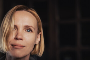 Fototapeta premium portrait of an attractive middle-aged woman with a slight smile, sadness in her eyes, looks into the camera on a dark background. Place for text.