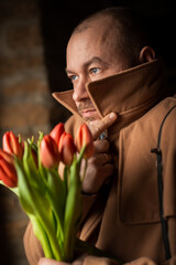 A man with a bouquet looks away in a dark room. Waiting for a meeting, a date.