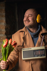 Funny look of a man with a bouquet, a retro radio and headphones in a coat. An absurd image for a...