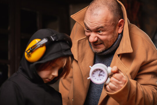 A man shakes an alarm clock in front of a young tired boy. The process of misperception concept.