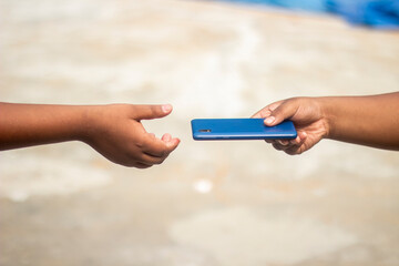 A boy hands a mobile phone to another person and the background is blurred behind them
