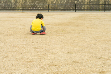 公園のグラウンドで一人座り込む小さな子供。いじける男の子。