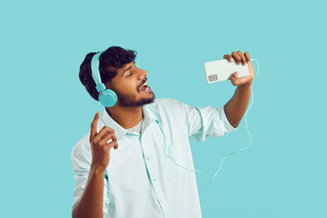 Cheerful Indian man listens to music in headphones and sings while recording his voice on mobile...