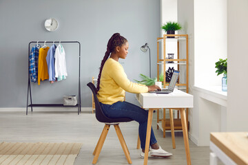 Side view of a young african american brunette business woman working with laptop computer at home or at ofiice and typing. Accountant freelancer considering new projects, analyzing company.