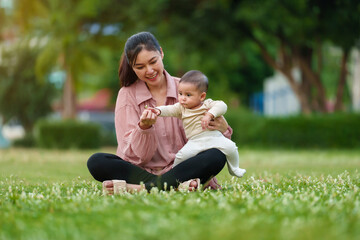 mother talking and playing with her infant baby while sitting on a grass field