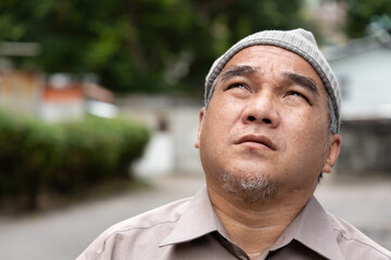 Old man cancer patient wearing grey chemotherapy hat, looking up and thinking after suffering from...