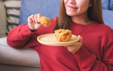 Closeup image of a young woman holding and eating fried chicken at home