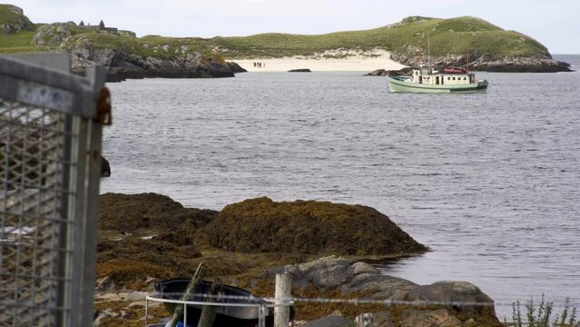 Static shot of a yacht anchored in the bay near a beach on Bernera. A group of people, seaweed and a cattle trailer are visible. Filmed on the Isle of Lewis, part of the Outer Hebrides.